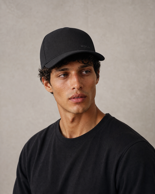 A man wearing the NOLL 01 silk-lined cap against a warm stone backdrop