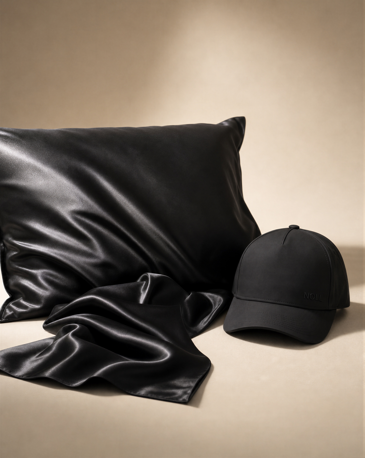 The black NOLL silk pillowcase beside the matte black NOLL 01 hat, with silk draped in front