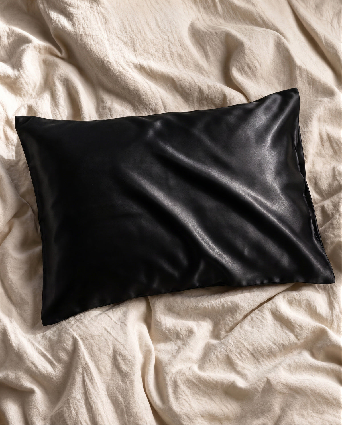 The black NOLL silk pillowcase on bone linen sheets, shot from above