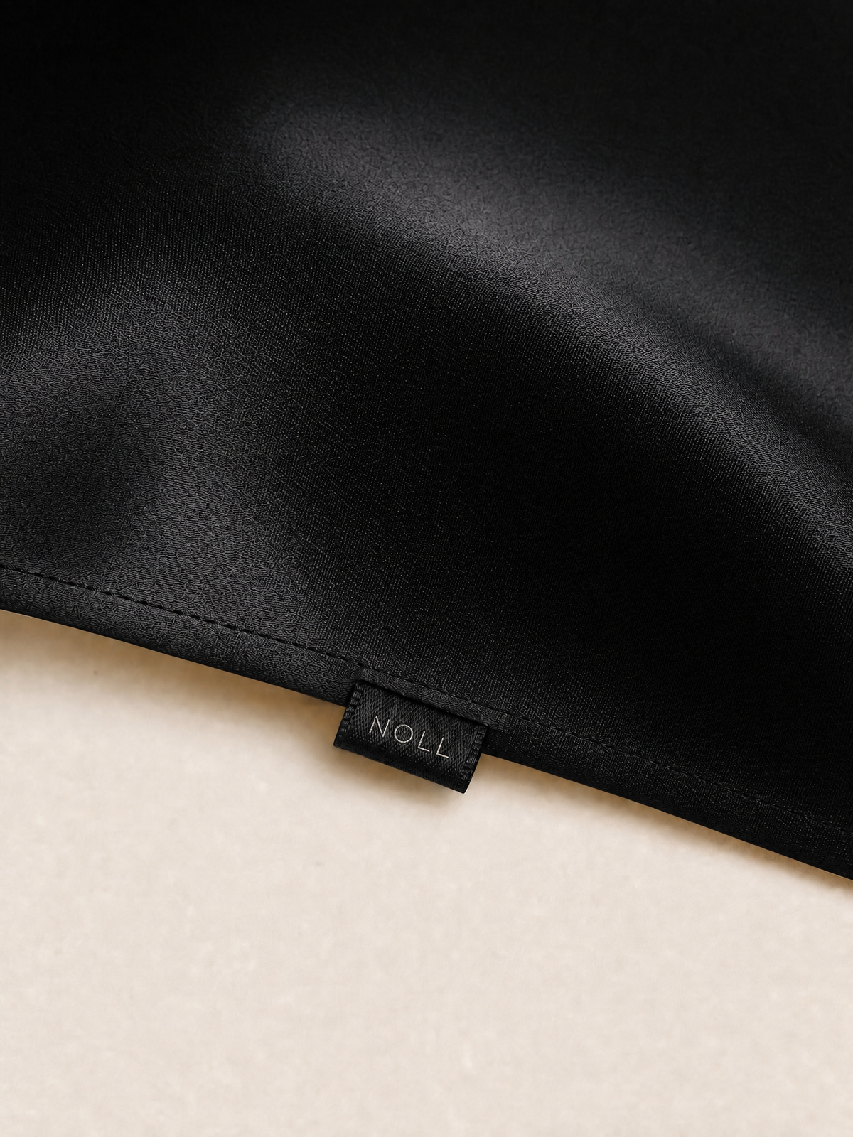 Close-up of the hemmed seam and the woven NOLL label on the black silk pillowcase